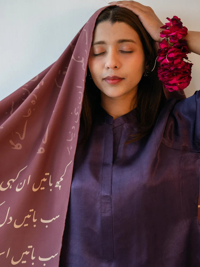 Mauve Ankahi Urdu poetry scarf draped loosely over the head beside a deep purple outfit, with pale calligraphy visible on the front panel.